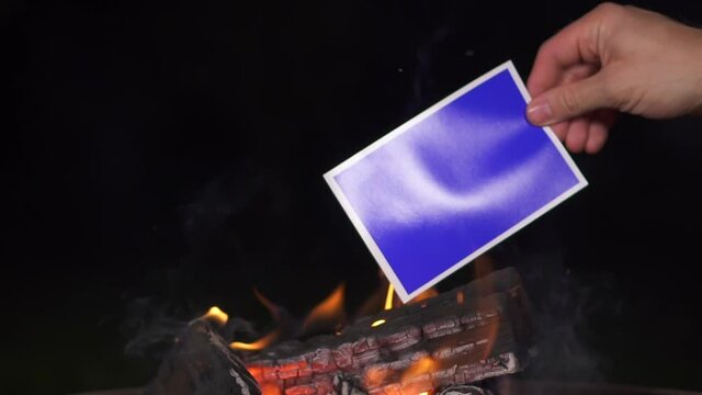 burn blue picture. place for your photo is on fire. throw photo in firewood fire in dark.chromakey black background. old blue card is burned out. background for your picture melts plastic