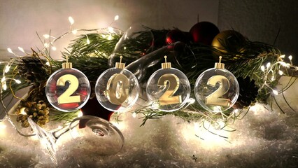 happy new year 2022 digits in transparent glass baubles on decoration with fairylights champagne...