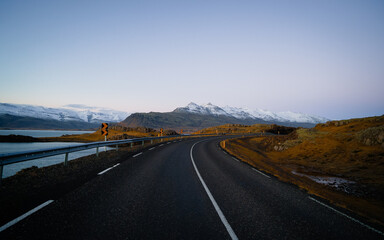 Empty road with Icelandic landscape during sunrise in the background mountains are covered by snow. Icelandic road on the country's East Coast