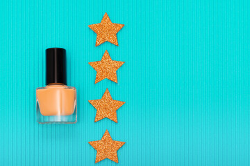 Orange nail polish bottle with orange Christmas stars on blue background. Beauty products concept....