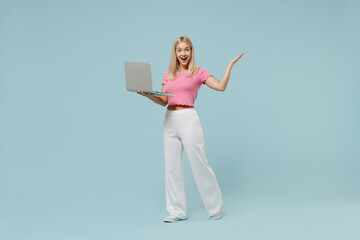 Full body young blonde woman 20s wearing casual pink t-shirt hold use work on laptop pc computer...