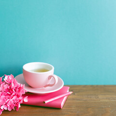 Pink diary, pencil, cup of tea, dry flowers on wooden table. mint blue wall background