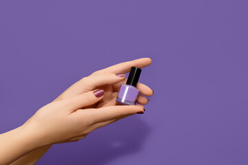 Female hands with red nail design. Glitter red nail polish manicure. Female hands hold purple nail polish on purple background.