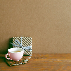 Gift box and cup of tea on wooden table. brown wall background. anniversary concept