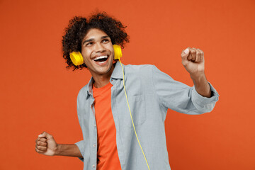 Young cheerful satisfied student black man 50s wearing blue shirt t-shirt headphones listen to music dance have fun isolated on plain orange color background studio portrait. People lifestyle concept.