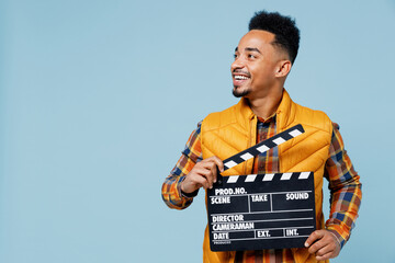 Jubilant exultant young black man 20s years old wear yellow waistcoat shirt looking aside holding classic black film making clapperboard isolated on plain pastel light blue background studio portrait - obrazy, fototapety, plakaty