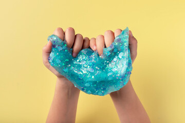 child playing with blue slime on yellow background. fun sensory toy for kids. Hands gum. closeup