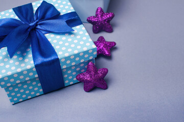 Blue gift box with a bow and violet stars on a gray background. Holiday greeting card.