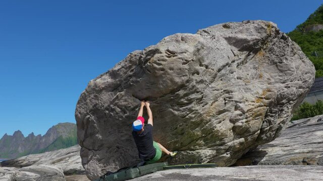 Young man bouldering on rock on Senja in norway with good weather and mountains in the background