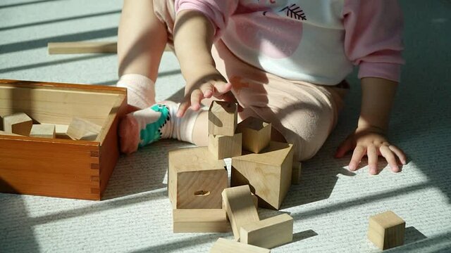 Hands of Toddler learning by stacking and balancing wooden blocks - multi-ethnic Korean-Ukrainian baby girl playing