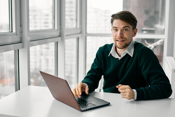 man in the office with an open laptop at the table near the window