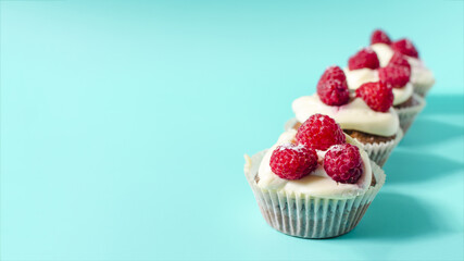 Sweet cupcakes with white cream and raspberries on a blue background sharpness in the foreground.