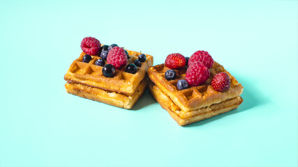 Soft waffles with a decor of black and red berries on a blue background close-up. Homemade cakes waffles on a colored background