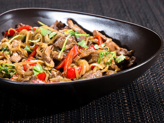 wok, stir fried noodle with beef sliced, bell pepper and parsley in soy sauce, served in a bowl