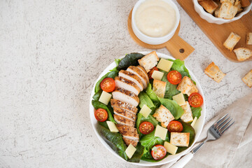 Caesar salad with chicken breast, cherry tomatoes, croutons and parmesan on a light background, top view