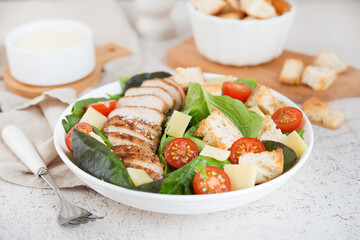 Caesar salad with chicken breast, cherry tomatoes, croutons and parmesan on a light background