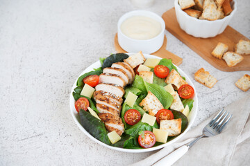 Caesar salad with chicken breast, cherry tomatoes, croutons and parmesan on a light background