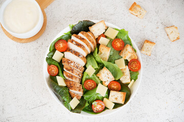 Caesar salad with chicken breast, cherry tomatoes, croutons and parmesan on a light background