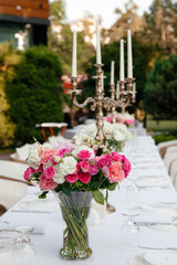 a bouquet of white roses, pink roses, pink carnations on a festive table with dishes decorated with large candelabra on a background of greenery of garden