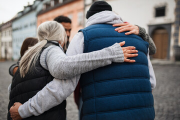 Rear view of community service volunteers hugging together outdoors in street