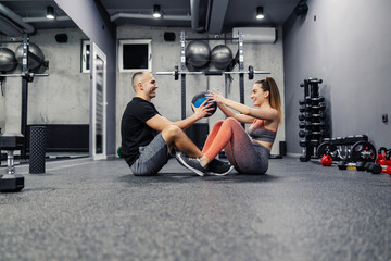 Fototapeta na wymiar Sit ups with a medicine ball. The concept of the interesting and different fitness training. The couple does sit-ups and throw a medicine ball at each other, abdominal exercises indoor gym