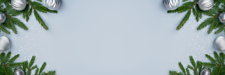 Christmas banner. Silver baubles and decorations, natural green fir tree branches and star shape confetti on light blue background. Winter season holiday layout. Copy space, top view, flat lay.