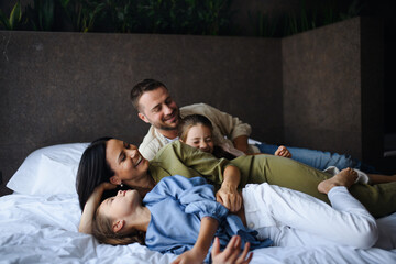 Happy young family with two children lying on bed at hotel, summer holiday.