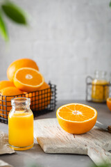 Organic homemade orange juice. Fresh juicy oranges in basket. Orange juice in bottles on gray stone background. Pile of oranges, Side view, copy space. Healthy eating diet, detox. Summer fruits.