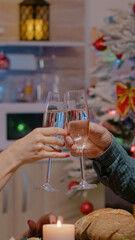 Festive couple enjoying christmas dinner and clinking glasses of champagne for winter celebration. Man and woman eating traditional food and drinking alcohol, celebrating festivity.