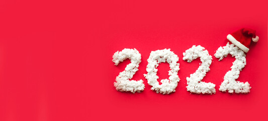 Happy new year concept 2022 with snow white numbers and santa hat on red background. banner