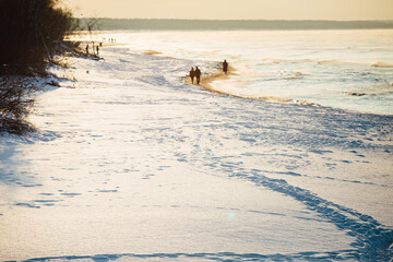 Winter color sunset at sea. A bright color sunset by the sea on a winter day. The beach is snowy. People walk along the sea. The beach is snowy.