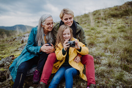 Small girl with mother and grandmother taking selfie pictures on top of mountain.