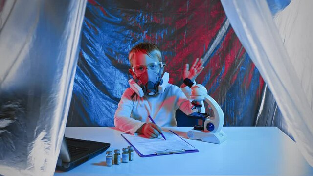 A little sientist with a microscope is writing down the results of his observations sitting at his desk in the laboratory