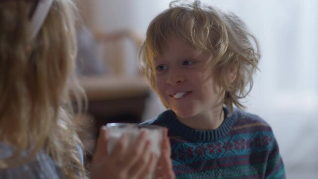 Portrait of cute joyful little boy drinking Christmas milk with girl smiling with white foam on lips. Happy relaxed carefree Caucasian children celebrating New Year at home indoors