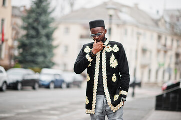 Mega stylish african man in traditional jacket pose. Fashionable black guy in hat and sunglasses with cigar in hand.