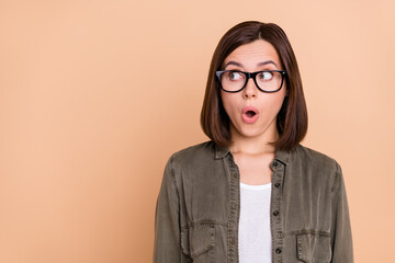 Photo of crazy lady look empty space unbelievable news wear specs khaki shirt isolated beige color background