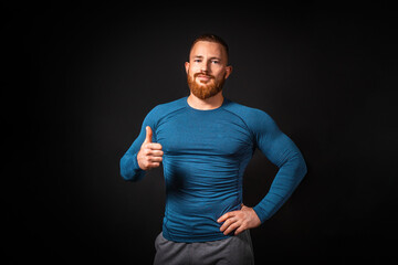 Handsome athletic muscular man showing a thumb up. Black background. Copy space. Sports advertising...
