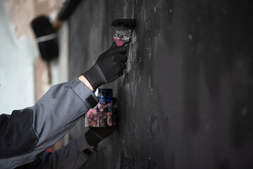 Worker painting the wall by the paint brush in the black color concept. Defocused photo.