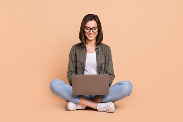 Photo of cheerful positive programmer lady sit floor hold pc wear eyewear khaki shirt isolated...