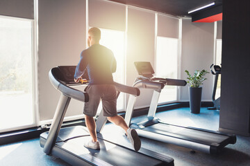 Fototapeta premium A sporty man runs on a treadmill in the gym. Keeping fit with cross training. Back view