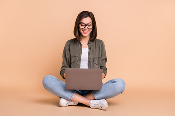 Photo of focused lady sit floor hold pc typing message email wear khaki shirt isolated beige color background
