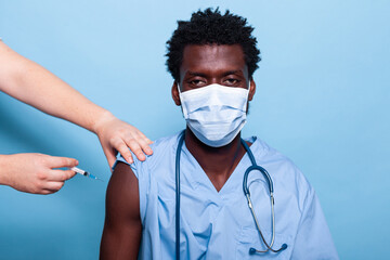 Black nurse getting vaccinated with syringe and needle while wearing face mask. African american healthcare assistant receiving vaccine shot from hands of doctor for virus protection