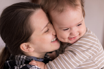 Portrait Adorable Face Of Little Cheerful Happy Toddler baby girl child With Charming Smile Look At Mom Strong Cuddles Loving Mommy Together. Mother Hugs play love care kiss smiling daughter at home