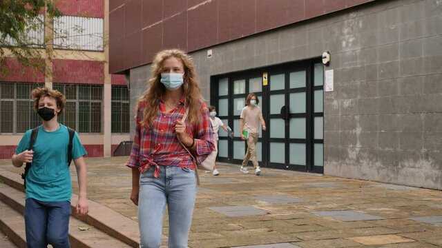 Teenager girl in face mask going home after classes in school with other teens who walking in background. . High quality 4k footage