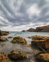 Fototapeta na wymiar There are several rocks in the foreground with silky water, a horizon bordered by a murky, moving sky. Cabo de Palos(Murcia-Spain)