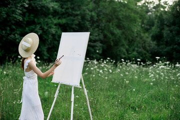 A woman in a white dress in a field with flowers paints a picture