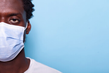 Close up of eye of african american person with face mask while looking at camera. Black face with protection against coronavirus epidemic for healthcare, standing over blue background