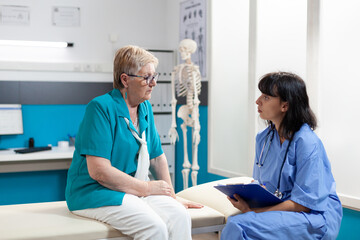 Medical assistant consulting aged woman with physical injury in office. Nurse doing examination for orthopedic diagnosis and recovery, talking about pain relief and physiotherapy