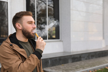 Handsome young man using disposable electronic cigarette outdoors