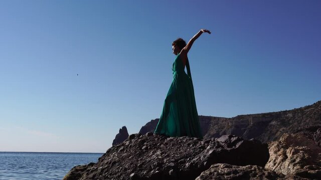 Side view a Young beautiful sensual woman with black hair in a long mint dress posing on a beach with calm sea bokeh lights on sunny day. Girl on the nature on blue sky background. Fashion photo